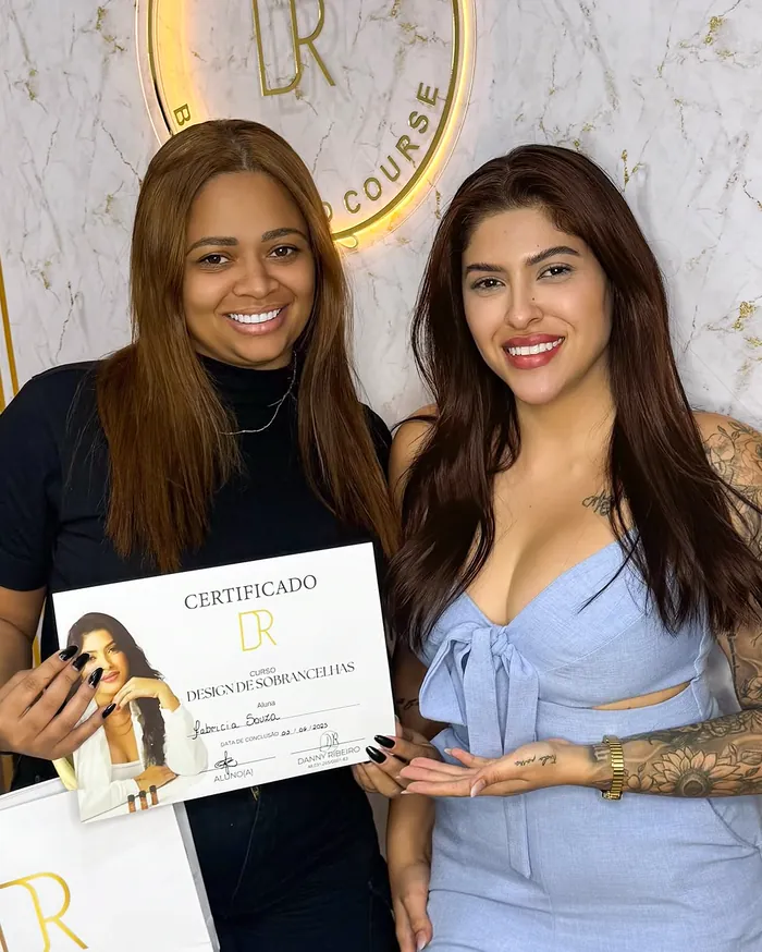 Aluna sorrindo com o certificado de design de sobrancelhas ao lado da Danny