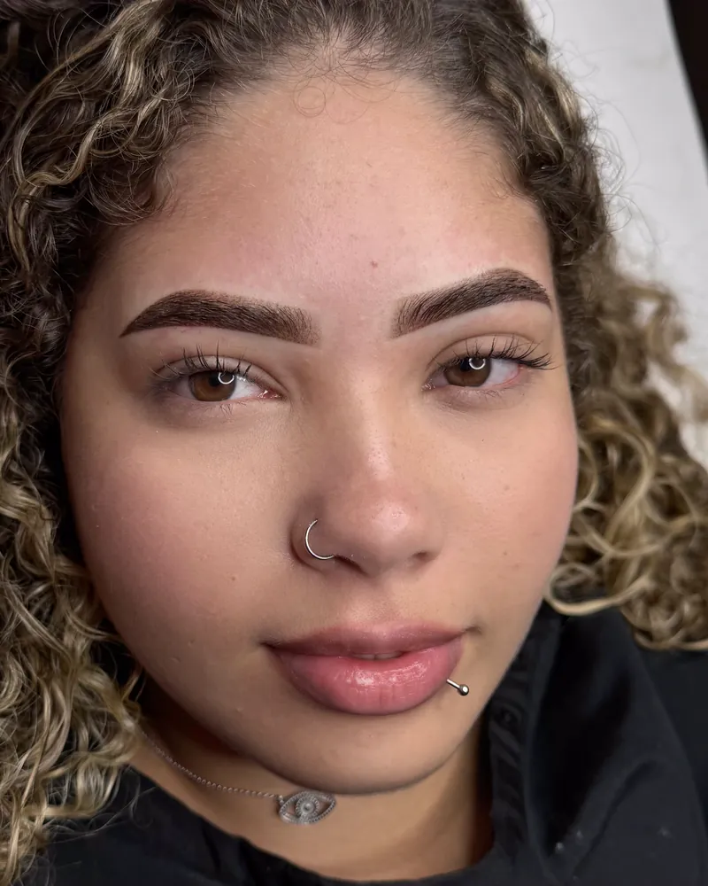 Cliente de cabelos cacheados com mechas loiras exibindo sobrancelhas com micropigmentação shadow