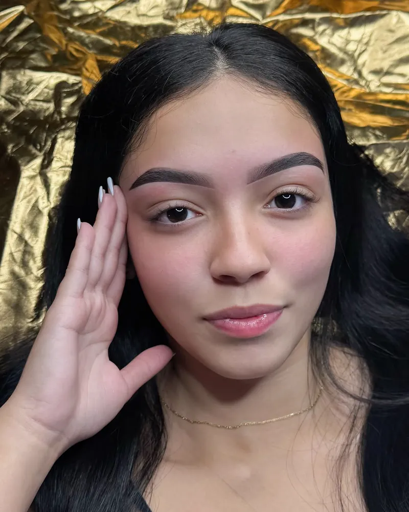 Cliente sobre fundo dourado com design de sobrancelhas e henna